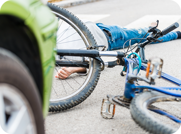 Photo of crashed bicycle and person laying on the ground with a car in the foreground