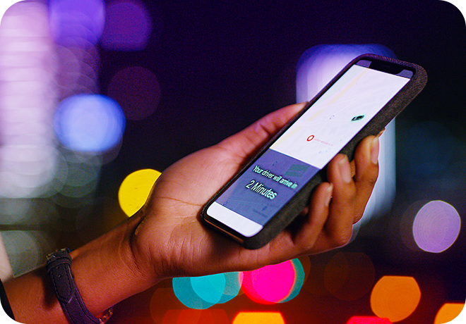 Photo of adult hand holding a mobile phone with a screen that says "Your driver will arrive in 2 minutes"