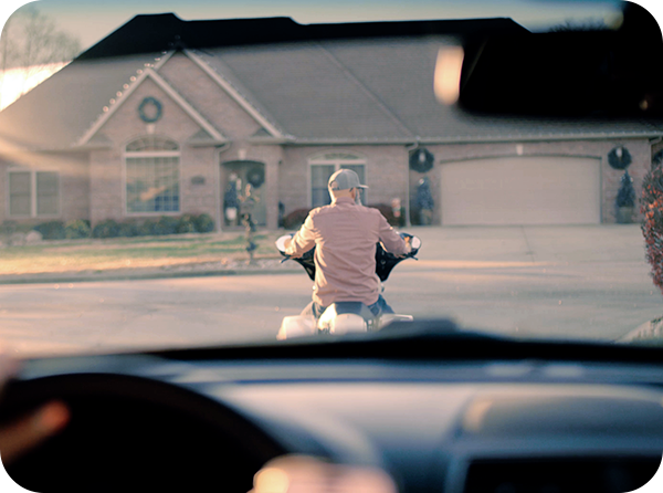 Photo from driver's perspective looking through the windshield at a man on a motorcycle stopped at a stop sign in front of the vehicle