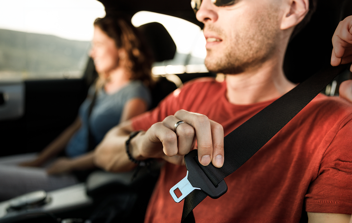 Photo of male driver putting his seat belt on with a woman in the background