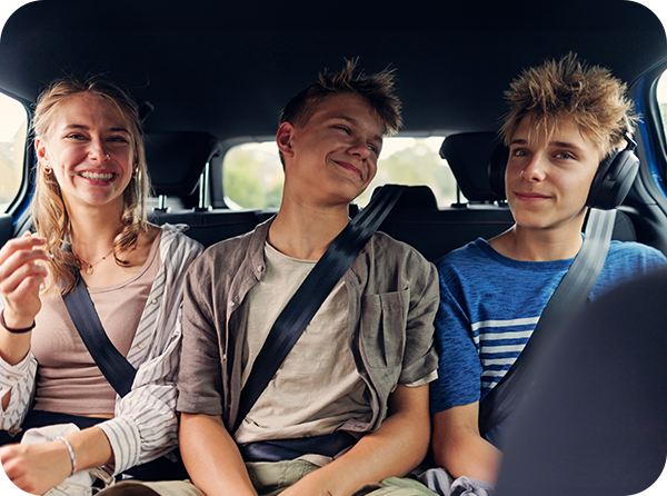 Photo of three teenagers in the back seat of a vehicle smiling with seat belts on