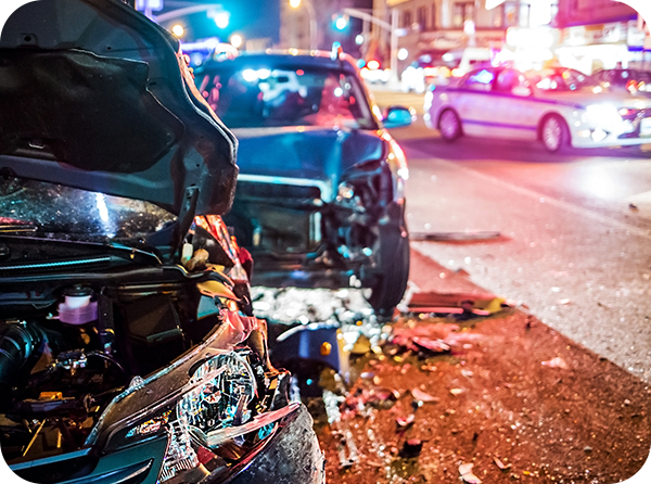 Photo of two crashed vehicles with police vehicles and flashing lights in the background