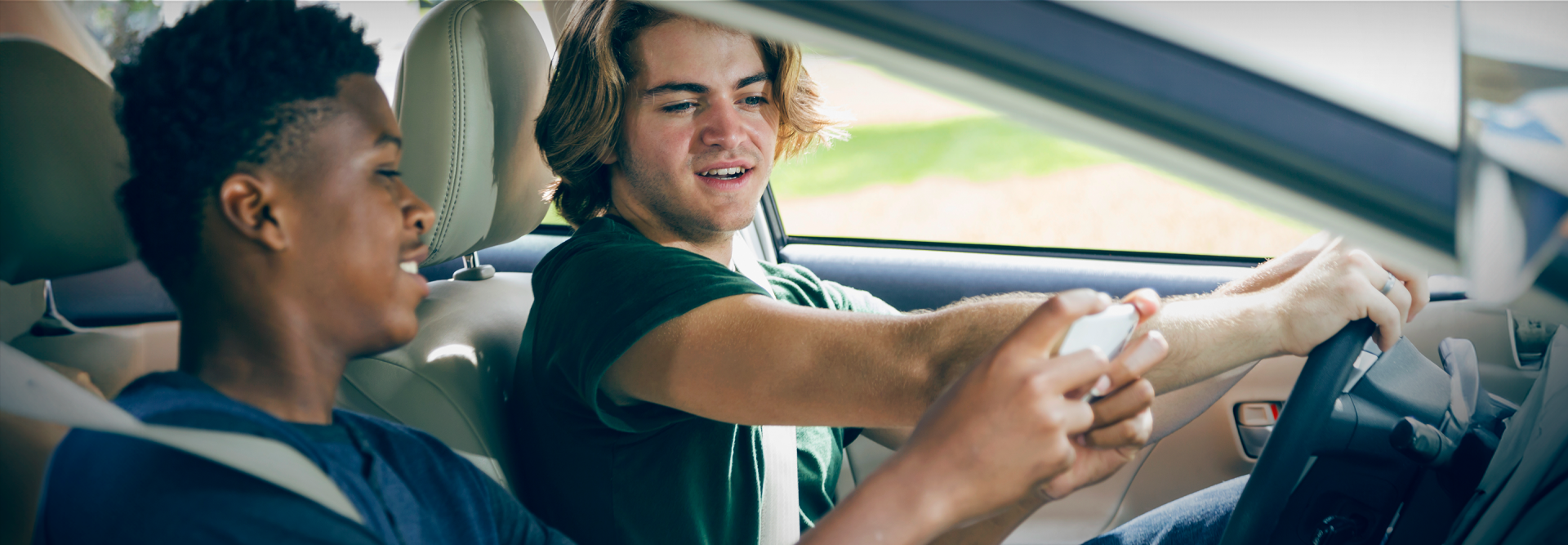 Photo of young driver looking at the phone of a young passenger while driving