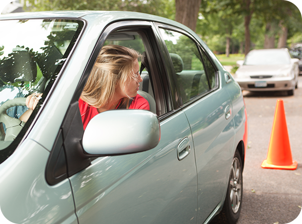 Photo of young driver presumably taking a driver's test looking over her shoulder as she reverses a vehicle