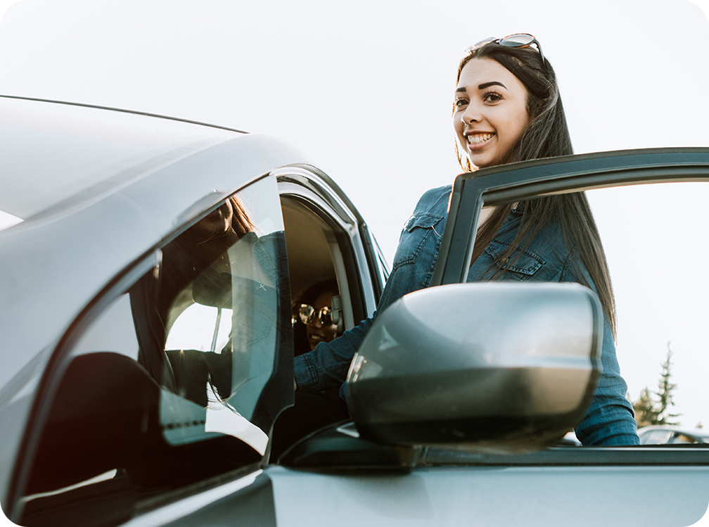 Photo of adolescent driver smiling at the camera and getting into her car