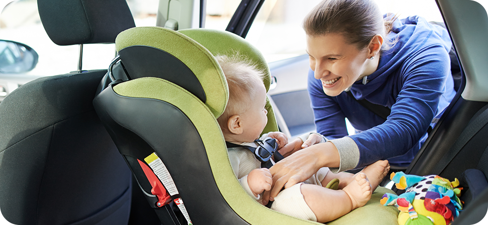 Photo of woman buckling her infant into a rear-facing infant car seat in the back seat of a vehicle