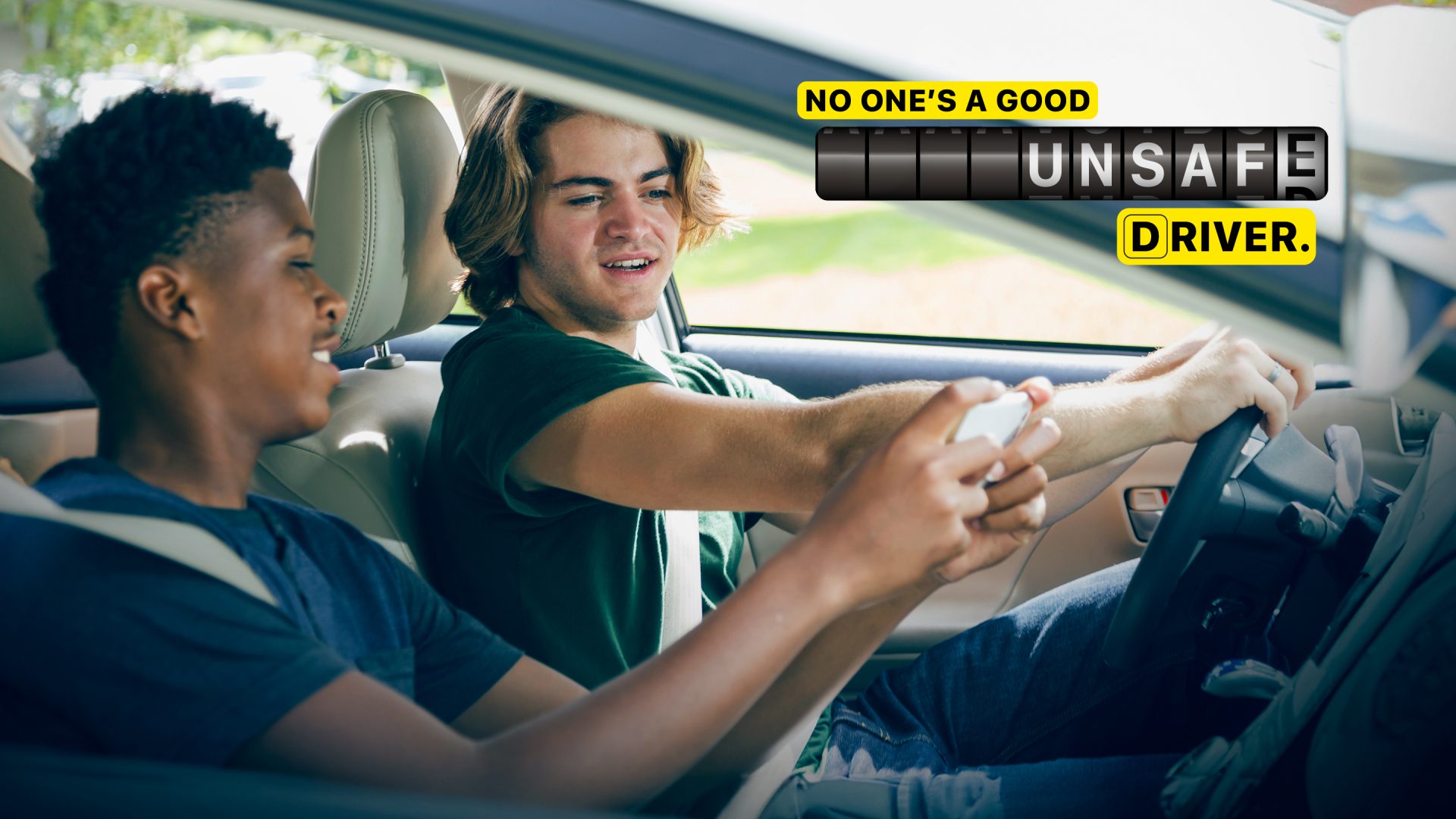 Photo of young driver looking at the phone of a young passenger while driving that says “No one’s a good unsafe driver”