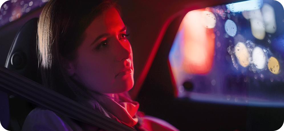 Photo of woman appearing sad presumably in the back seat of a police vehicle with red and blue lights in the background