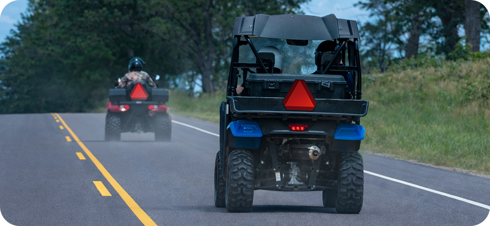 Two all-terrain vehicles (ATVs) on a public road with slow-moving vehicle signs.